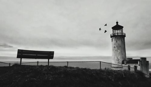 Lighthouse on beach against cloudy sky