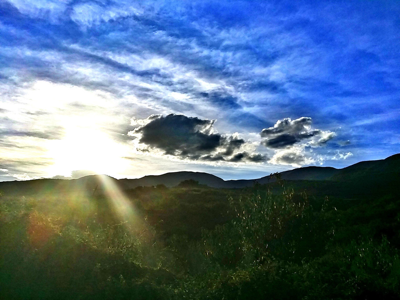 mountain, sky, tranquil scene, tranquility, scenics, landscape, beauty in nature, cloud - sky, sunbeam, mountain range, sun, nature, sunlight, cloud, non-urban scene, grass, cloudy, idyllic, blue, lens flare