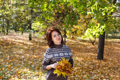 Beautiful young woman with light brown hair in sweater on background of foliage