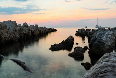 Rocks in sea against sky during sunset