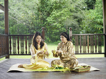 Mother and daughter weaving leaves in gazebo at yard