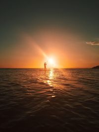 Silhouette man paddleboarding on sea against sky during sunset