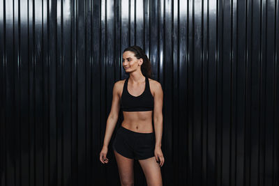 Young female athlete in sports clothing standing by corrugated iron