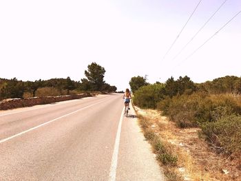 Rear view of woman riding bicycle on road against sky