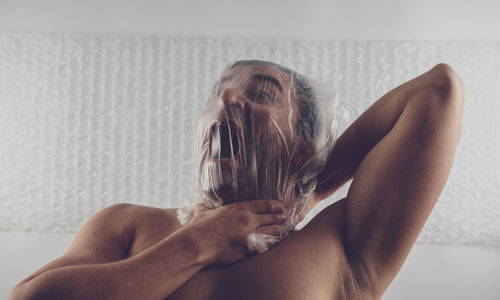 Man strangling neck with plastic bag against wall
