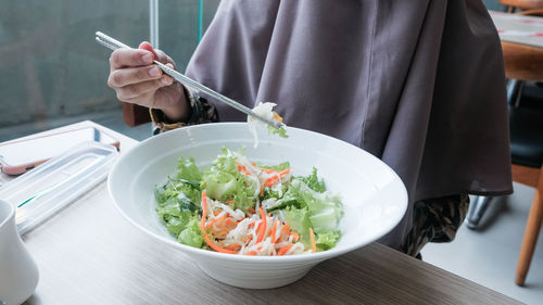 Midsection of man holding salad in bowl on table