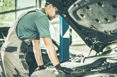 Side view of mechanic repairing car at garage