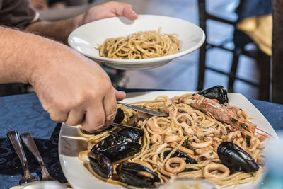 Close-up of hand taking noodles in plate on table