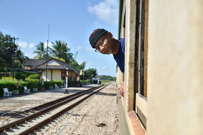 Man and railroad tracks by building against sky