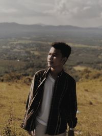 Young man looking away while standing on land