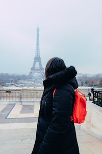 Side view of backpack woman standing against eiffel tower