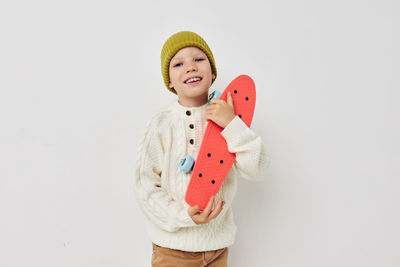 Portrait of smiling girl holding skateboard against white background