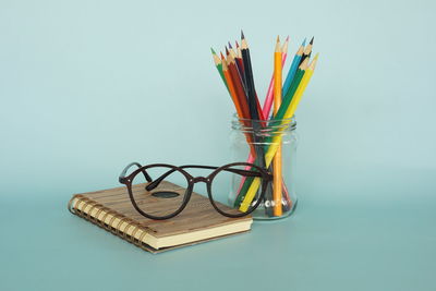 Close-up of multi colored pencils on glass table against blue background