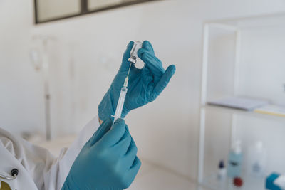 Close-up of doctor filling syringe with covid-19 vaccine at examination room