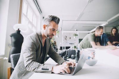 Confident businessman using laptop at desk in creative office