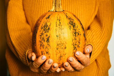 Pumpkin in the hands of woman with orange warm autumn cozy woolen sweater