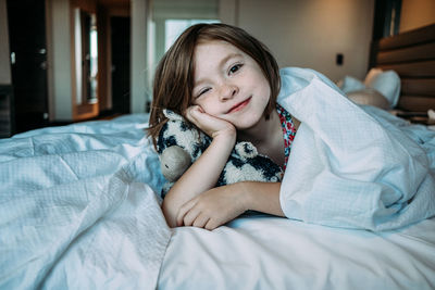 Straight on of young girl laying in a bed with her stuffed animal