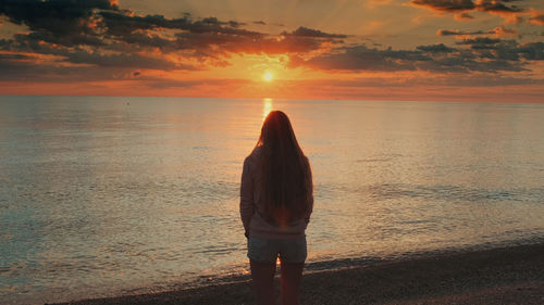 Rear view of woman standing on beach during sunset