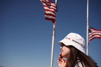 Low angle view of woman wearing hat with flag in air against blue sky