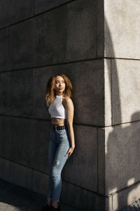 Portrait of young woman standing against wall