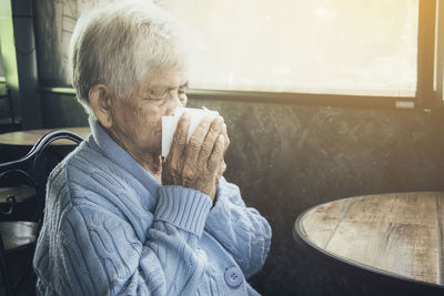 Old person coughing covering mouth with a tissue on a house interior. she has flu, allergy symptoms.