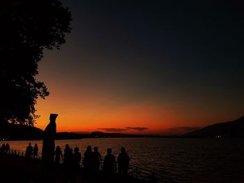 Silhouette people by sea against sky during sunset