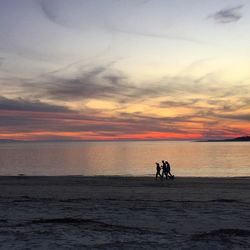 Silhouette people walking at beach against sky during sunset