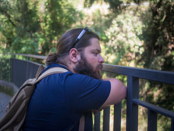 Portrait of young man on railing against trees