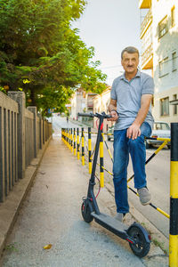 Portrait of man holding push scooter sitting on railing in city