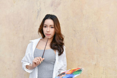 Young woman holding colorful palate against wall