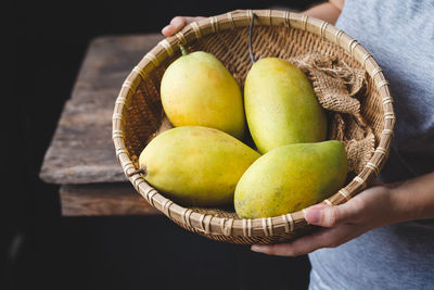 Midsection of woman holding mangoes in basket over table