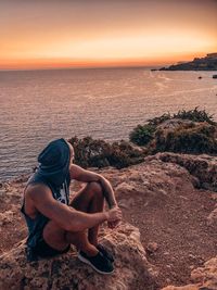 Full length of man sitting on rock at beach