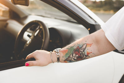 Cropped image of tattooed hand on car