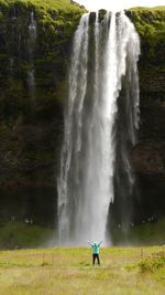 Scenic view of waterfall with woman standing on grass