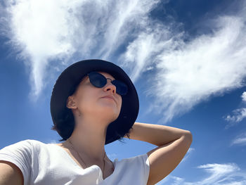 Summer portrait of young woman in panama hat with blue cloudy sky on background. side view of young