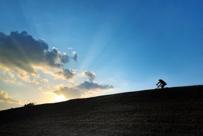 Silhouette man riding bicycle on road against sky during sunset