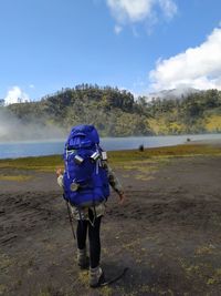 Rear view of person with backpack on land against sky