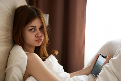 Young woman looking away while sitting on bed at home