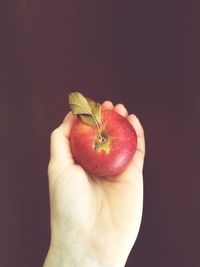 Close-up of hand holding strawberry over black background