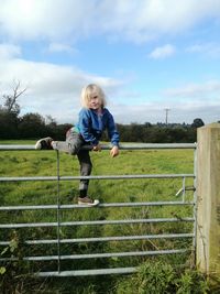 Full length of boy climbing gate against sky