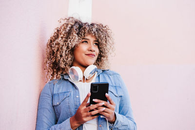 Young woman using mobile phone against wall