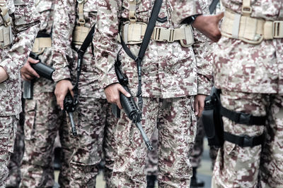 Midsection of army soldiers with machine guns standing outdoors