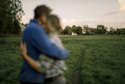 Couple hugging each other with agricultural field in background during sunset