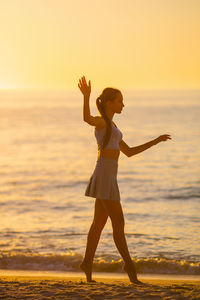 Side view of woman with arms outstretched standing at beach during sunset