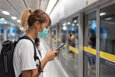 Woman using mobile phone while standing waiting for train 