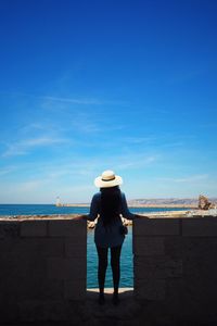 Rear view of woman standing amidst surrounding wall by sea against sky