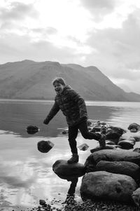 Full length of boy on rock by lake against sky