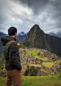 Man pointing at old ruins while standing on mountain against sky