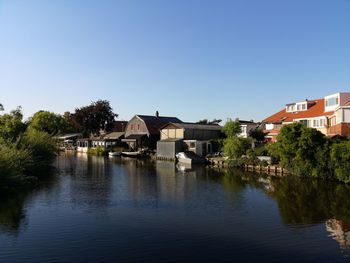 Buildings by river against clear blue sky