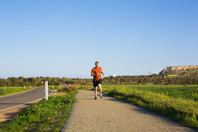 Rear view of man running on road against clear blue sky